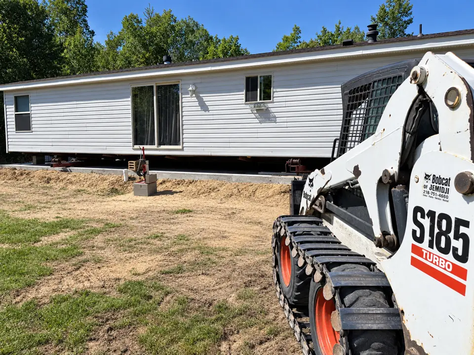 Skid-steer with forks beside a manufactured home